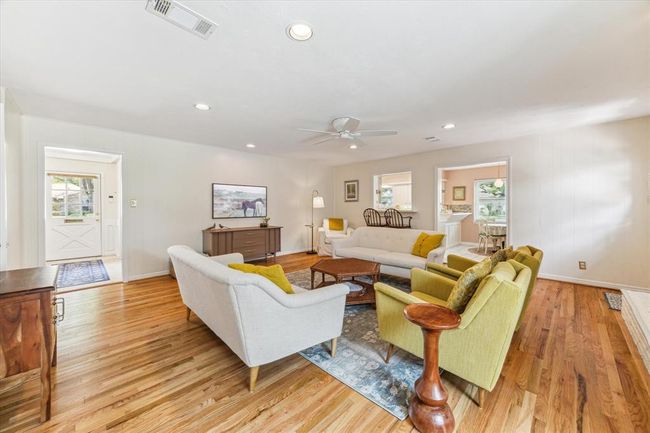 Experience the inviting charm of this family room, featuring classic hardwood floors and recessed lighting, seamlessly connected to the kitchen. | Image 9