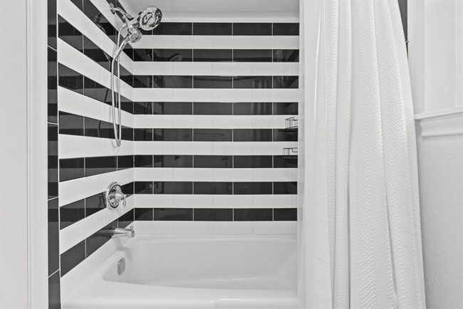 This bathroom features a modern tub and shower with a black and white striped tile design, complemented by a sleek, handheld shower head. | Image 29