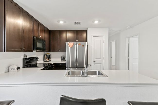 Kitchen with black appliances, dark brown cabinetry, light countertops, recessed lighting, and a peninsula | Image 14
