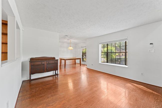 Bright, open living space with hardwood floors, large windows offering natural light, and a cozy dining area. Features built-in shelving and a classic sideboard for added charm. | Image 6