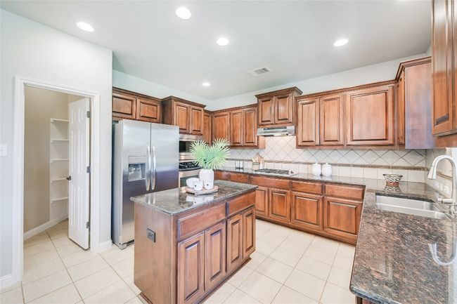 Kitchen with stainless steel appliances, brown cabinets, recessed lighting, light tile patterned floors, and dark stone countertops | Image 5
