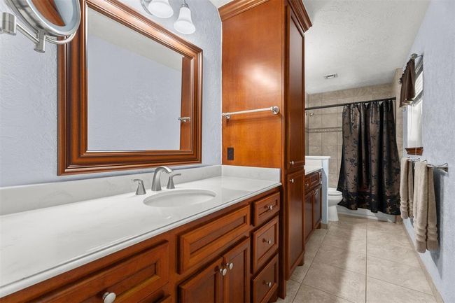 This bathroom features a sleek marble countertop with an under-mount sink, complemented by rich wood cabinetry. each side has a large mirror, modern fixtures, and a tiled shower area. The space is well-lit and has a clean, contemporary look. | Image 21