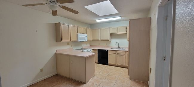 Kitchen featuring white appliances, a skylight, a sink, a ceiling fan, and light tile patterned floors | Image 8