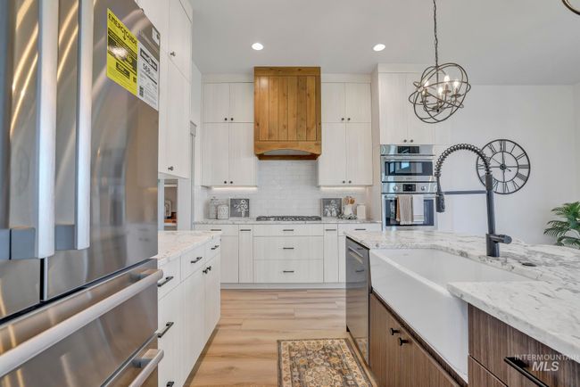 Kitchen with stainless steel appliances, white cabinetry, backsplash, hanging light fixtures, and light wood-style flooring | Image 13