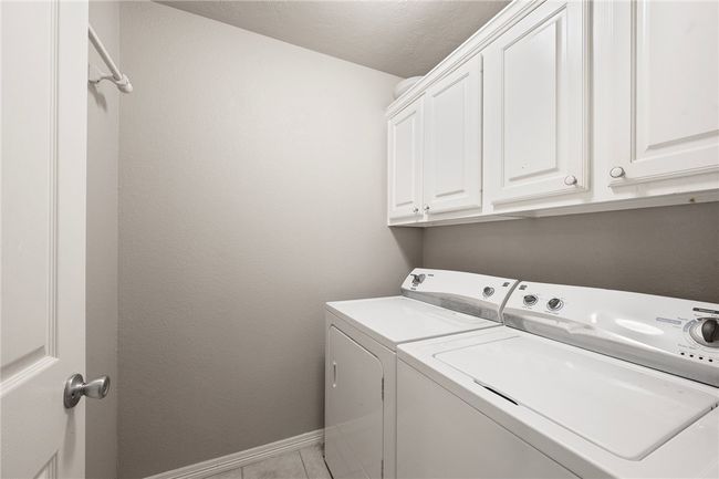 Laundry room with separate washer and dryer, cabinet space, baseboards, light tile patterned floors, and a textured ceiling | Image 5