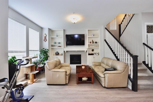 Living area with stairs, light wood finished floors, a fireplace, and built in shelves | Image 16