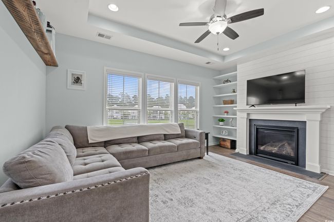 Open Concept living area on the second level featuring recessed lighting, a tray ceiling, ceiling fan, large gas fireplace and large windows with a pond view. | Image 22