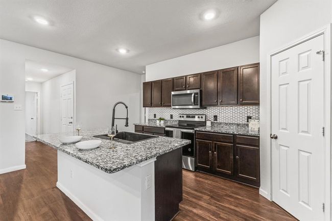 Kitchen with stainless steel appliances, dark wood-style flooring, tasteful backsplash, light stone counters, and a kitchen island with sink | Image 5