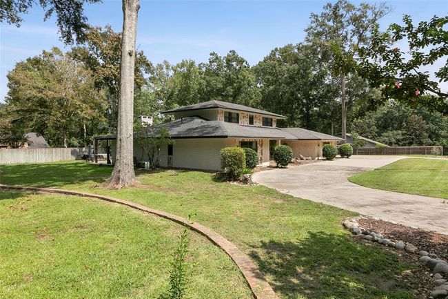 Charming two-story home with a spacious driveway and lush green surroundings, featuring mature trees and a well-maintained lawn. The property offers ample outdoor space and privacy with a fenced yard, ideal for family living. | Image 6