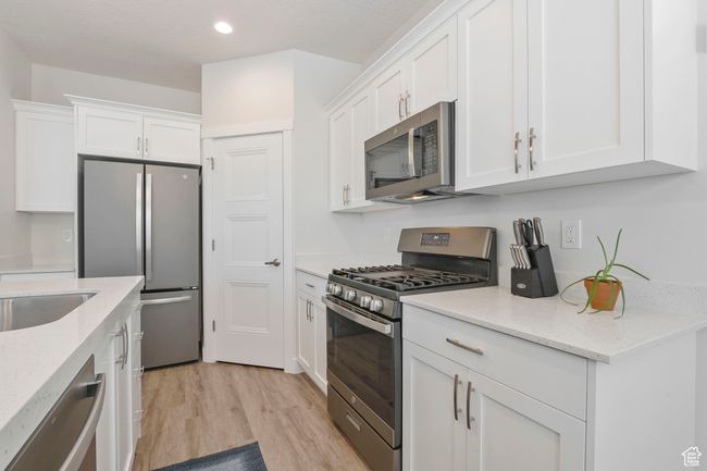 Kitchen with stainless steel appliances, white cabinetry, light wood-style flooring, recessed lighting, and light stone counters | Image 10