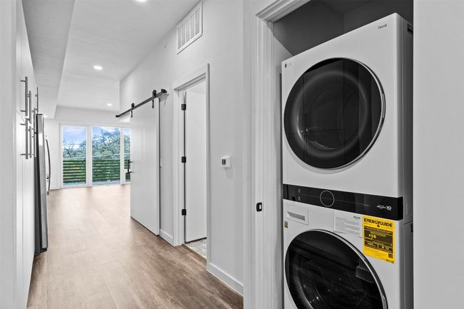 Laundry area with stacked washer and clothes dryer, a barn door, light wood-type flooring, recessed lighting, and baseboards | Image 5