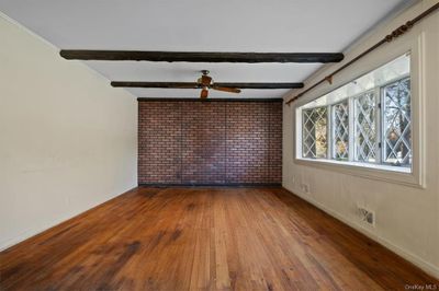 Unfurnished room featuring ceiling fan, beamed ceiling, hardwood / wood-style flooring, ornamental molding, and brick wall | Image 3