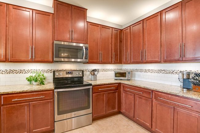 Kitchen with stainless steel appliances, decorative backsplash, light stone counters, and light tile patterned floors | Image 6