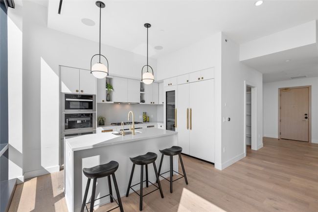 Kitchen featuring light wood finished floors, light countertops, a kitchen breakfast bar, white cabinetry, and hanging light fixtures | Image 5