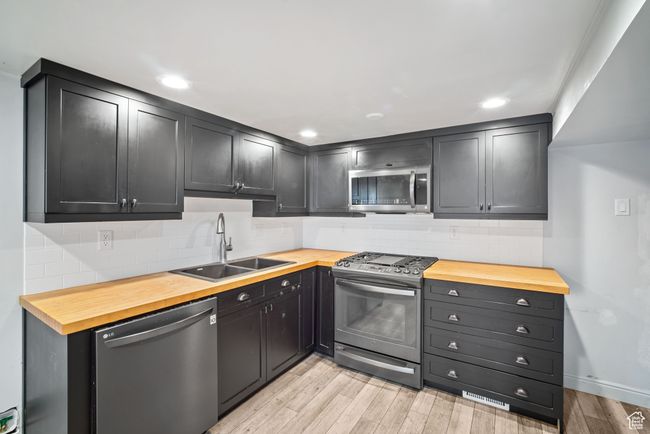 Kitchen with stainless steel appliances, wood counters, a sink, light wood-type flooring, and backsplash | Image 15