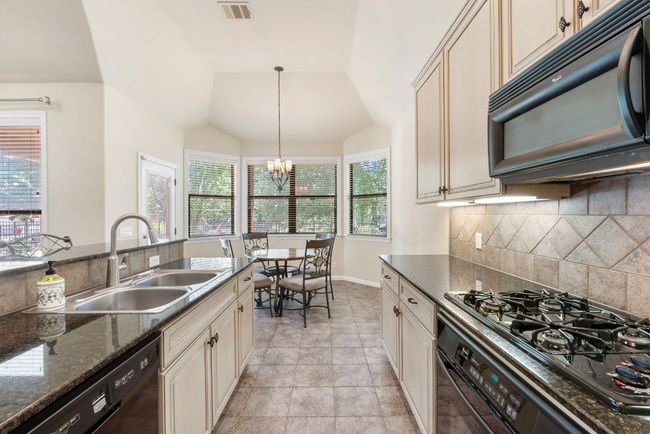 Kitchen with black appliances, cream cabinets, tasteful backsplash, a chandelier, and vaulted ceiling | Image 12