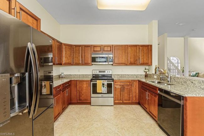 Kitchen featuring a sink, light stone counters, a peninsula, appliances with stainless steel finishes, and brown cabinetry | Image 4