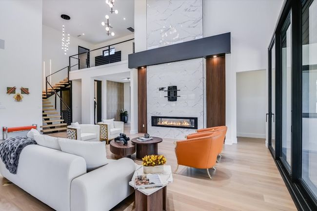 Living area featuring a high ceiling, open floating stairway, wood finished floors, and a stunning marble fireplace | Image 12