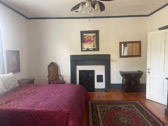Bedroom featuring wood finished floors, ornamental molding, a fireplace with flush hearth, and ceiling fan | Image 21