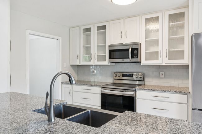 Kitchen with appliances with stainless steel finishes, decorative backsplash, light stone counters, and white cabinetry | Image 6