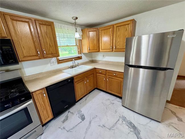 Kitchen with black appliances, a sink, light marble finish floors, brown cabinetry, and a textured ceiling | Image 24