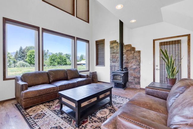 Living area featuring a wood stove, plenty of natural light, baseboards, light wood-style floors, and high vaulted ceiling | Image 16
