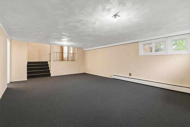 Below grade area featuring stairway, a baseboard radiator, dark colored carpet, baseboards, and a textured ceiling | Image 10