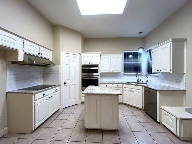 Kitchen with stainless steel appliances, under cabinet range hood, decorative backsplash, and white cabinets | Image 9