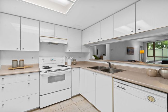 Kitchen featuring white appliances, under cabinet range hood, a sink, and light countertops | Image 8