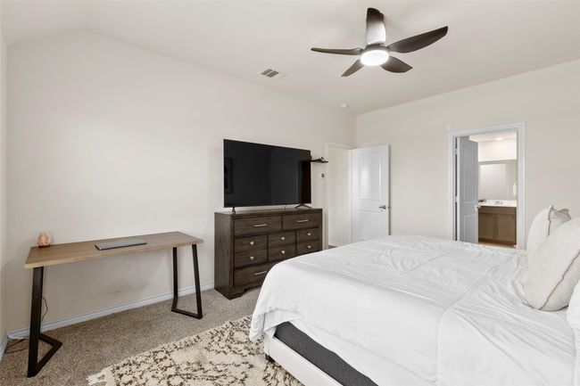 Carpeted bedroom with vaulted ceiling, connected bathroom, ceiling fan, baseboards, and visible vents | Image 18