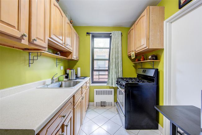 Kitchen with gas stove, radiator heating unit, light brown cabinetry, light tile patterned floors, and open shelves | Image 12