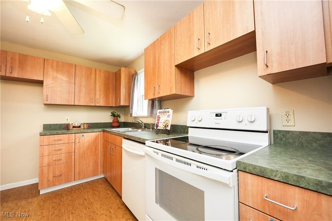 Kitchen with dark countertops, a ceiling fan, a sink, and white appliances | Image 11