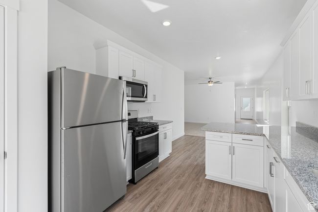 Kitchen featuring ceiling fan, appliances with stainless steel finishes, light wood-style floors, a peninsula, and white cabinetry | Image 5