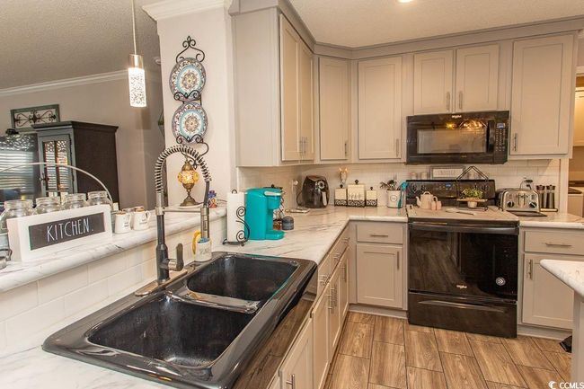 Kitchen with a textured ceiling, crown molding, a sink, black appliances, and backsplash | Image 10