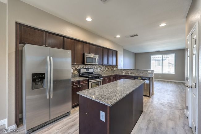 Kitchen featuring backsplash, a kitchen island, light stone countertops, appliances with stainless steel finishes, and dark brown cabinets | Image 24