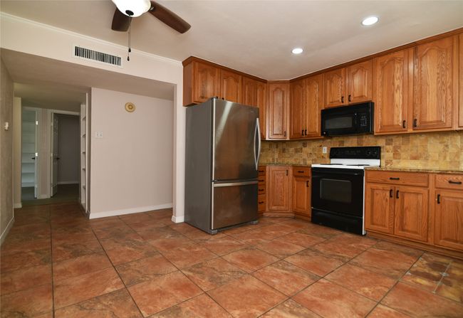 Kitchen featuring freestanding refrigerator, electric stove, black microwave, decorative backsplash, and baseboards | Image 10