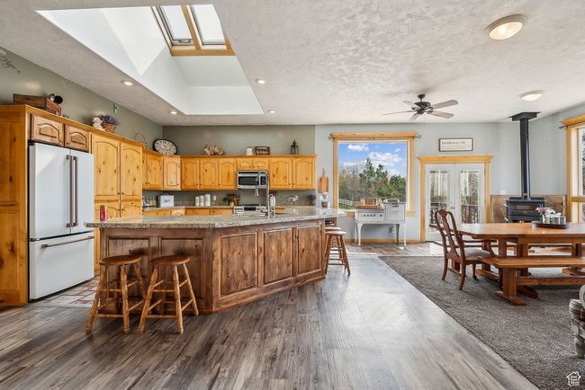 Kitchen with an island with sink, dark wood-style floors, a wood stove, appliances with stainless steel finishes, and ceiling fan | Image 11