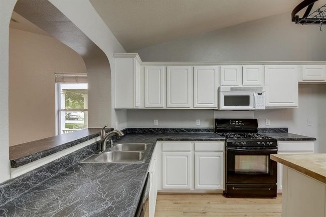 Kitchen with black range with gas stovetop, white microwave, lofted ceiling, a sink, and light wood-style flooring | Image 10