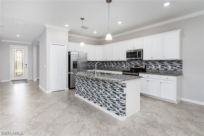 Kitchen with decorative light fixtures, dark stone counters, a kitchen island with sink, appliances with stainless steel finishes, and sink | Image 5