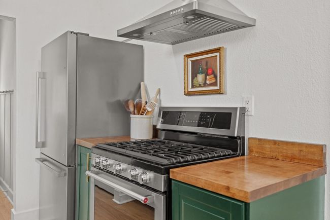 Kitchen featuring green cabinets, appliances with stainless steel finishes, butcher block countertops, wall range hood, and light wood-style flooring | Image 10
