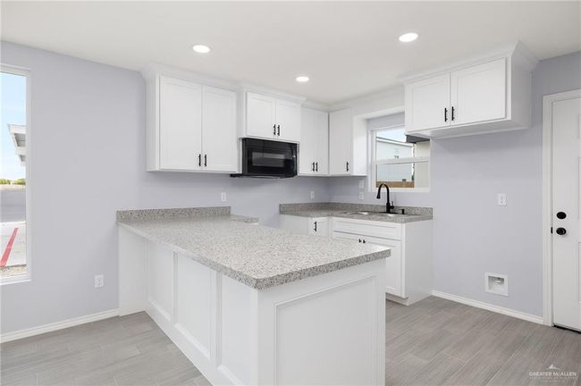 Kitchen with black microwave, a sink, baseboards, wood finish floors, and white cabinetry | Image 5
