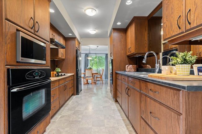 Kitchen featuring black appliances, brown cabinetry, dark countertops, range hood, and recessed lighting | Image 27