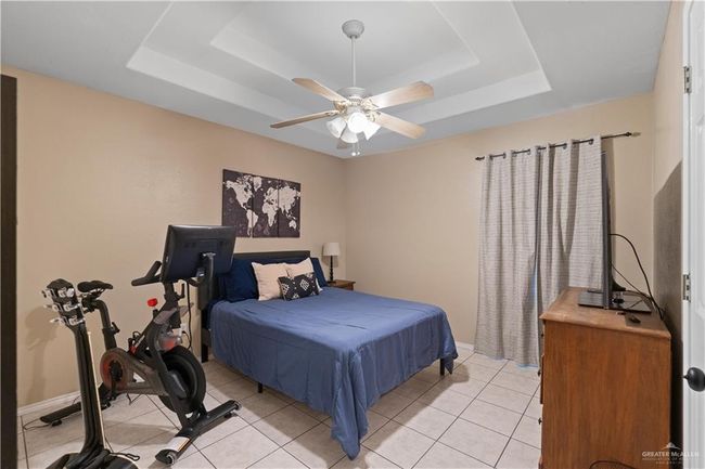Bedroom with a tray ceiling, light tile patterned floors, baseboards, and ceiling fan | Image 5