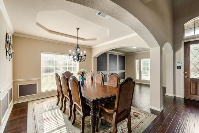 Dining space featuring a tray ceiling, dark wood-type flooring, arched walkways, a chandelier, and crown molding | Image 19