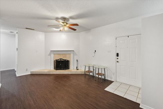 Unfurnished living room featuring wood finished floors, a ceiling fan, a tiled fireplace, and a textured ceiling | Image 6