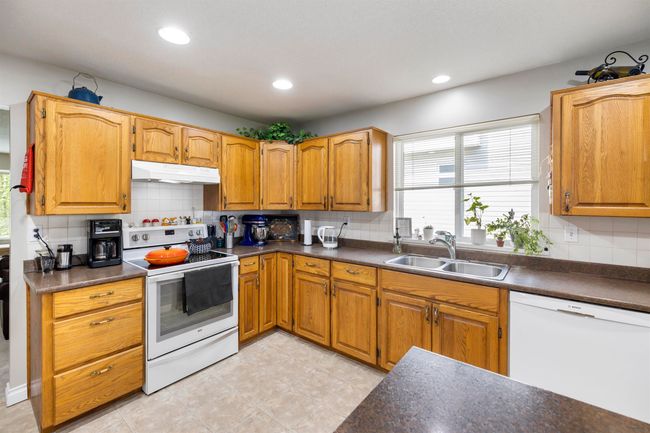 Kitchen featuring under cabinet range hood, white appliances, a sink, and dark countertops | Image 8