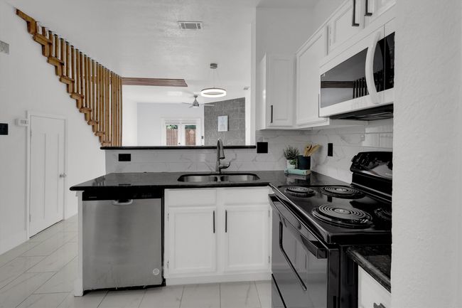 Kitchen featuring black electric range oven, decorative backsplash, white cabinetry, and stainless steel dishwasher | Image 4