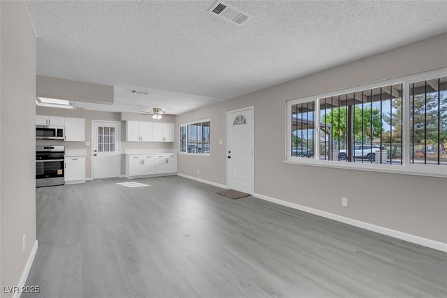 Unfurnished living room with wood finished floors, visible vents, baseboards, a textured ceiling, and ceiling fan | Image 9