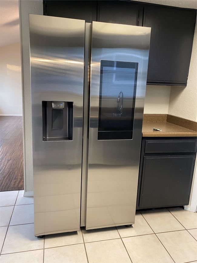 Kitchen with stainless steel fridge with ice dispenser, light tile patterned floors, dark countertops, and dark cabinets | Image 16