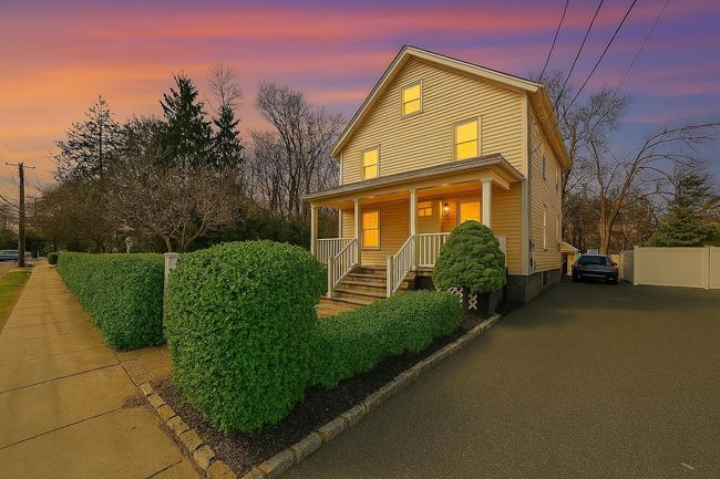 Traditional home with covered porch, driveway, and bushes. Digitally enhanced | Image 4